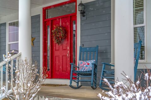 bright red front door with rockers on front porch and snow covered bushes