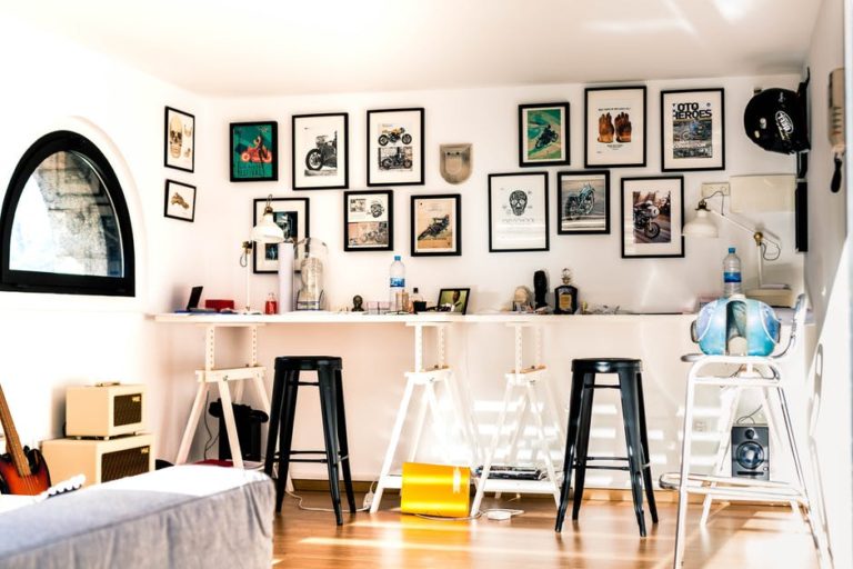 Wall with lots of picture frames and a desk with lots of stools underneath the pictures